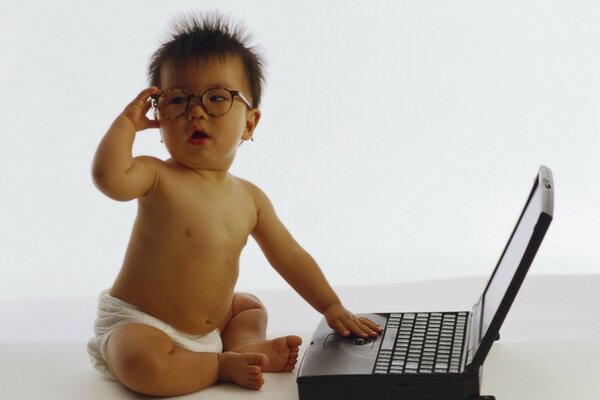 Piccolo bambino con gli occhiali seduto al computer portatile