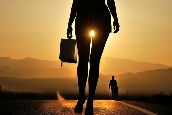 Siluetta della ragazza con la valigia al tramonto