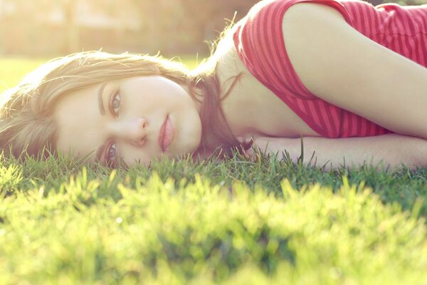Ragazza in posa sdraiata su una radura verde bagnata dal sole