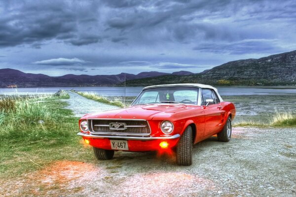 Mustang rosso vicino al lago con tempo nuvoloso