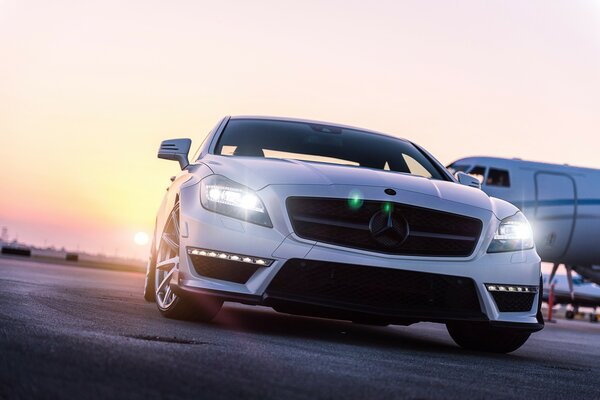 Mercedes di colore bianco in aeroporto sullo sfondo di un aereo