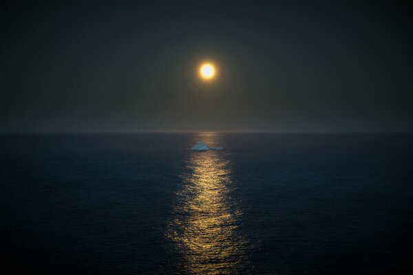 In mezzo al mare, un iceberg galleggia alla luce della luna piena