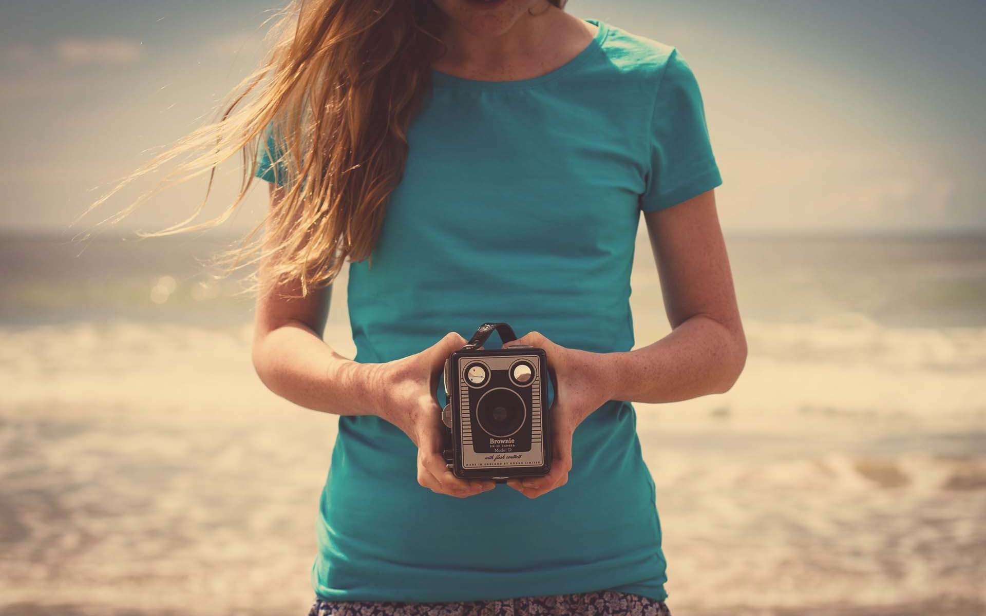 umore ragazza capelli scuri natura spiaggia sabbia mani macchina fotografica macchina fotografica sfondo. carta da parati carta da parati