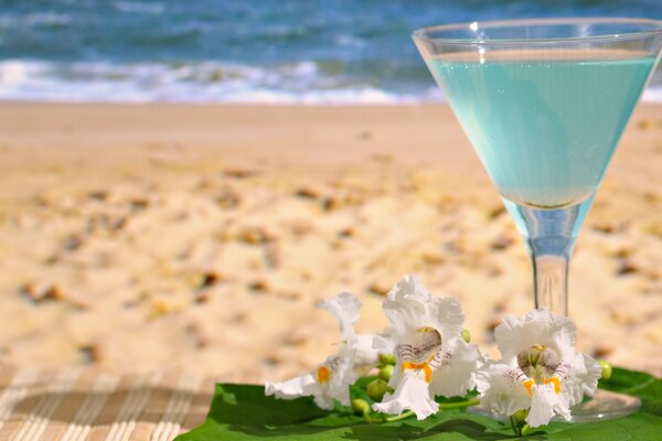 Bicchiere con bevanda e fiori sullo sfondo della spiaggia di mare