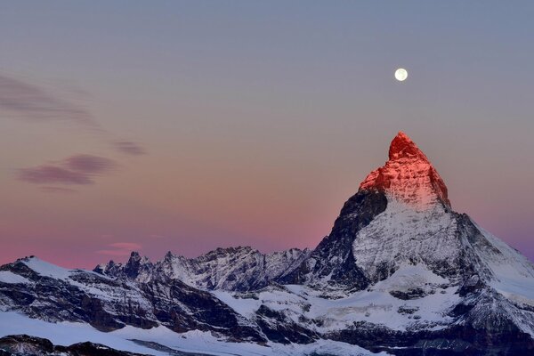 Cima delle Alpi sullo sfondo del cielo crepuscolare. Luna sopra la cima